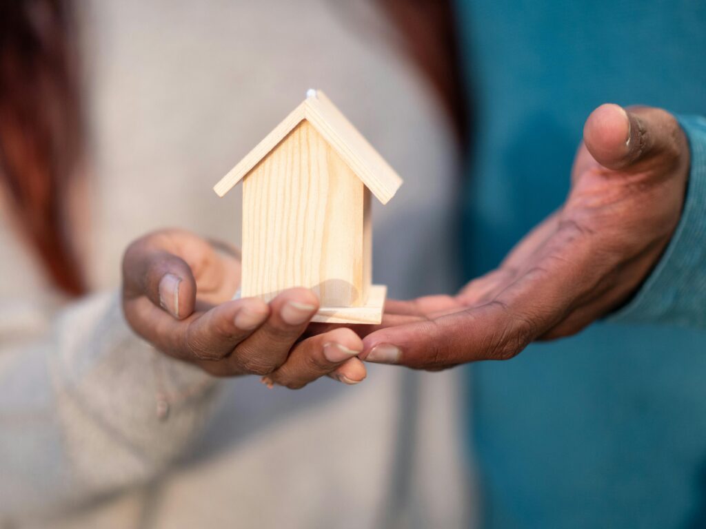Close-up of hands holding a miniature wooden house, symbolizing home ownership and real estate investment.