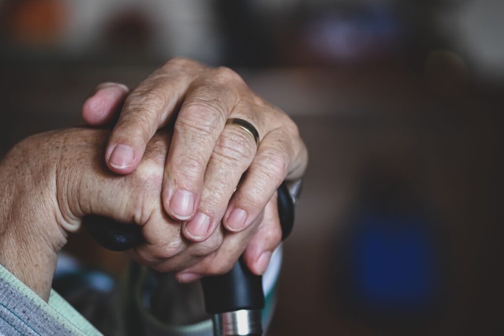 Close-up of senior hands clasped around a cane, highlighting a wedding ring, symbolizing love and support.