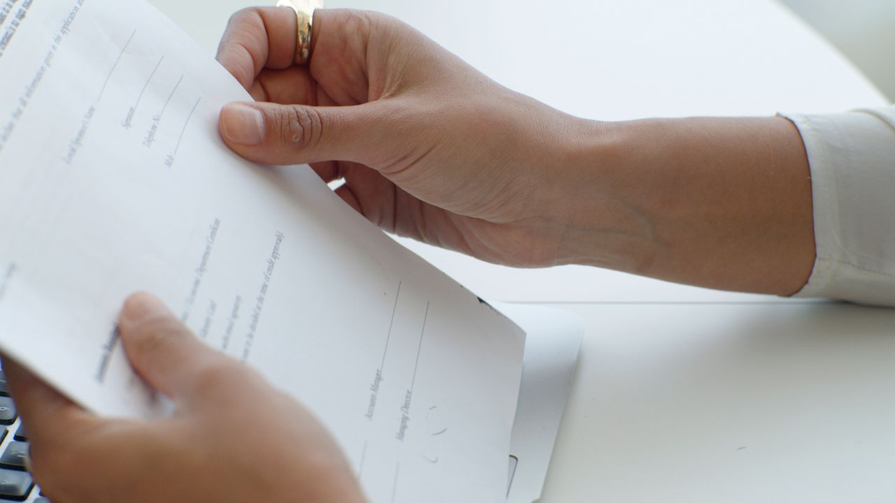 Close-up view of hands holding a document over a keyboard in an office.