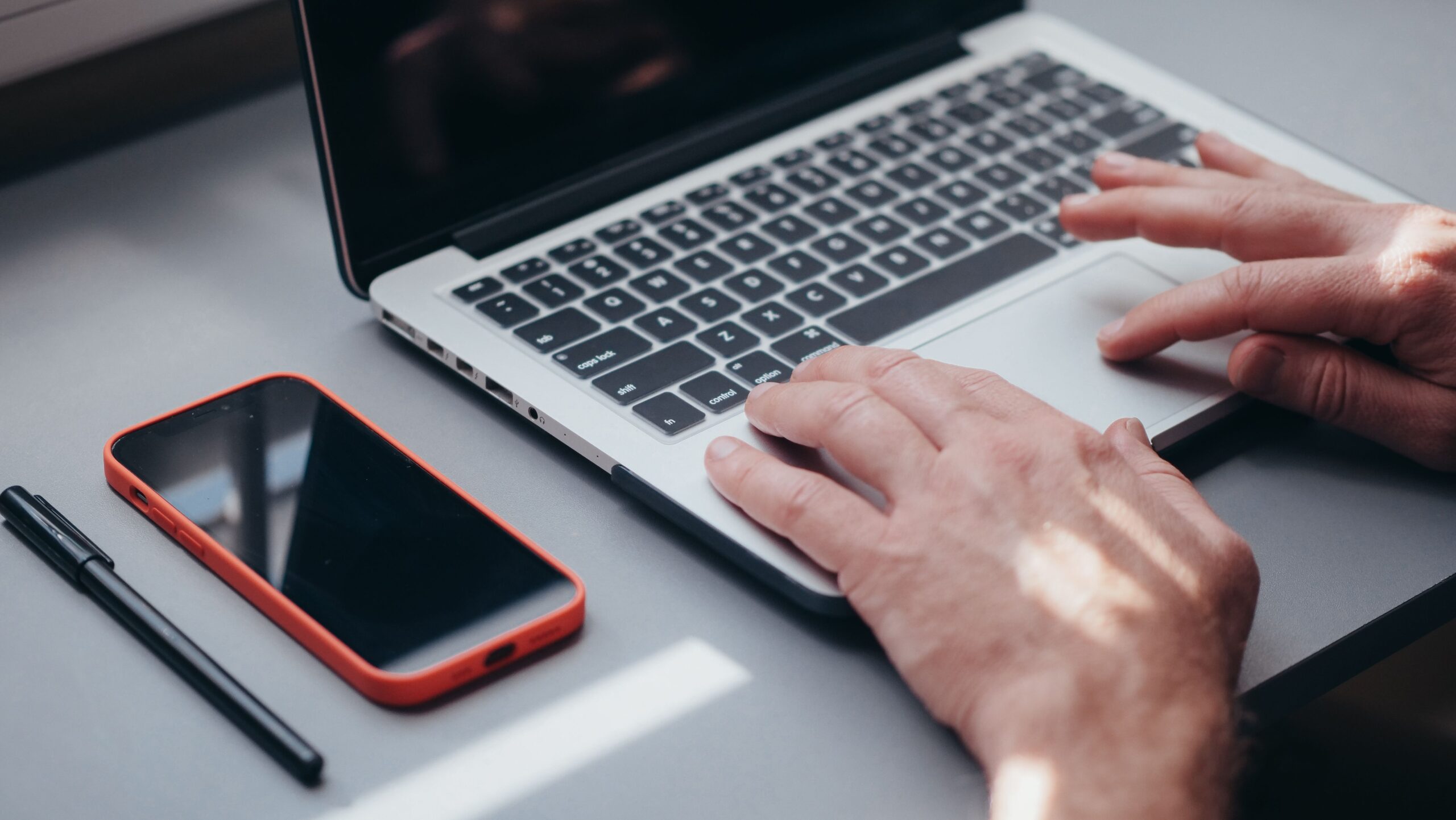 Hands typing on a laptop with a smartphone and pen on the side, perfect for tech and work themes.